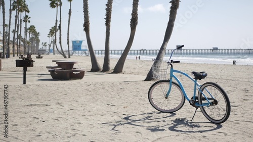 Blue bicycle, cruiser bike by sandy ocean beach, pacific coast near Oceanside pier, California USA. Summertime vacations, sea shore. Vintage cycle, tropical palm trees, lifeguard tower watchtower hut