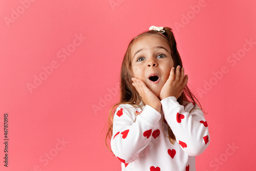 Cute young girl on pink background making surprised face photo