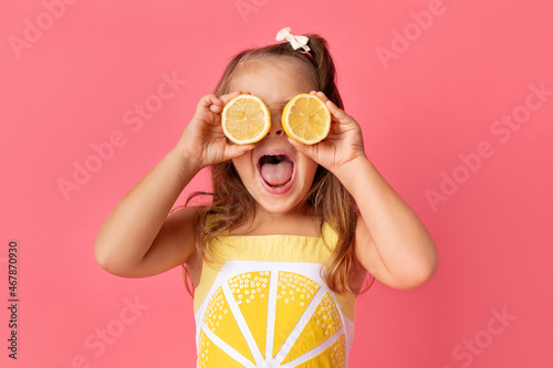 Funny young girl on pink background holding lemons against her eyes photo