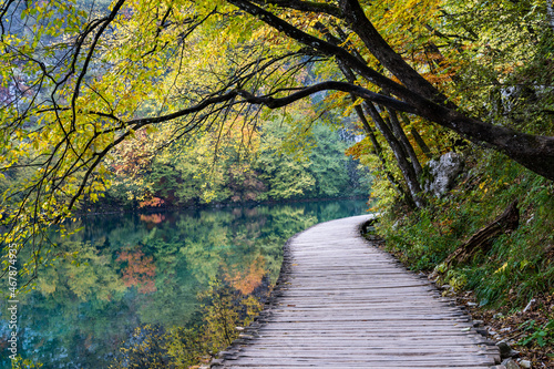rustic wooden boardwalk leading along the shores of a picturesque mountain lake with trees and foliage in intense fall colors