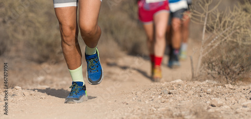 Group of young adults competition and running together through trails on the hillside outdoors in nature. People trail running on a mountain path