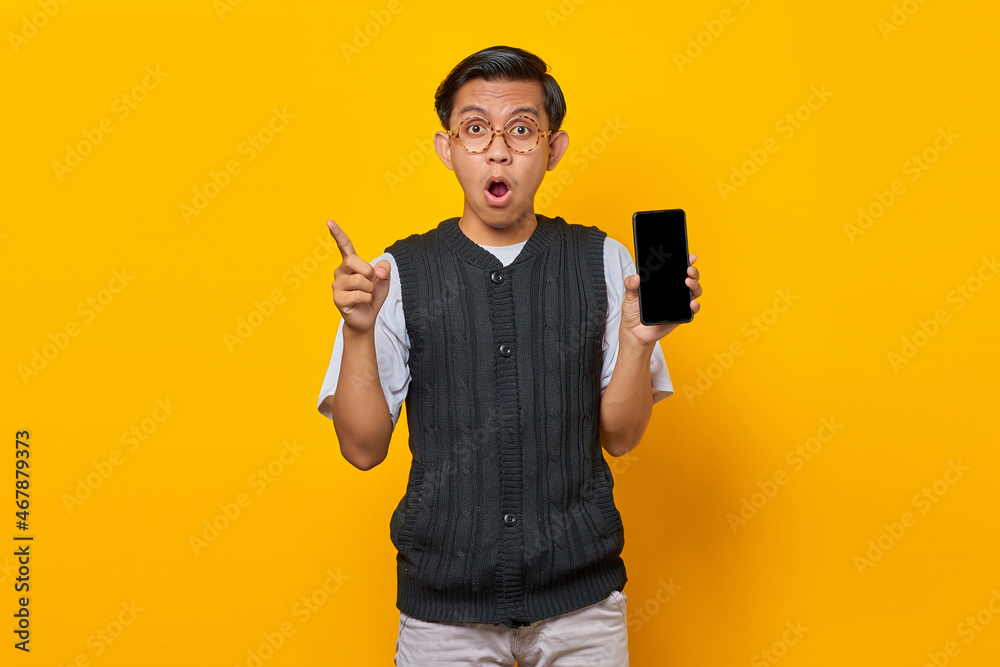 Shocked Asian man showing blank smartphone screen and finger pointing at empty space Shocked Asian man showing blank smartphone screen and finger pointing at empty space