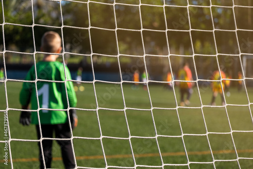 Rear view behind the net of a child football goalkeeper in the goal. Blur background