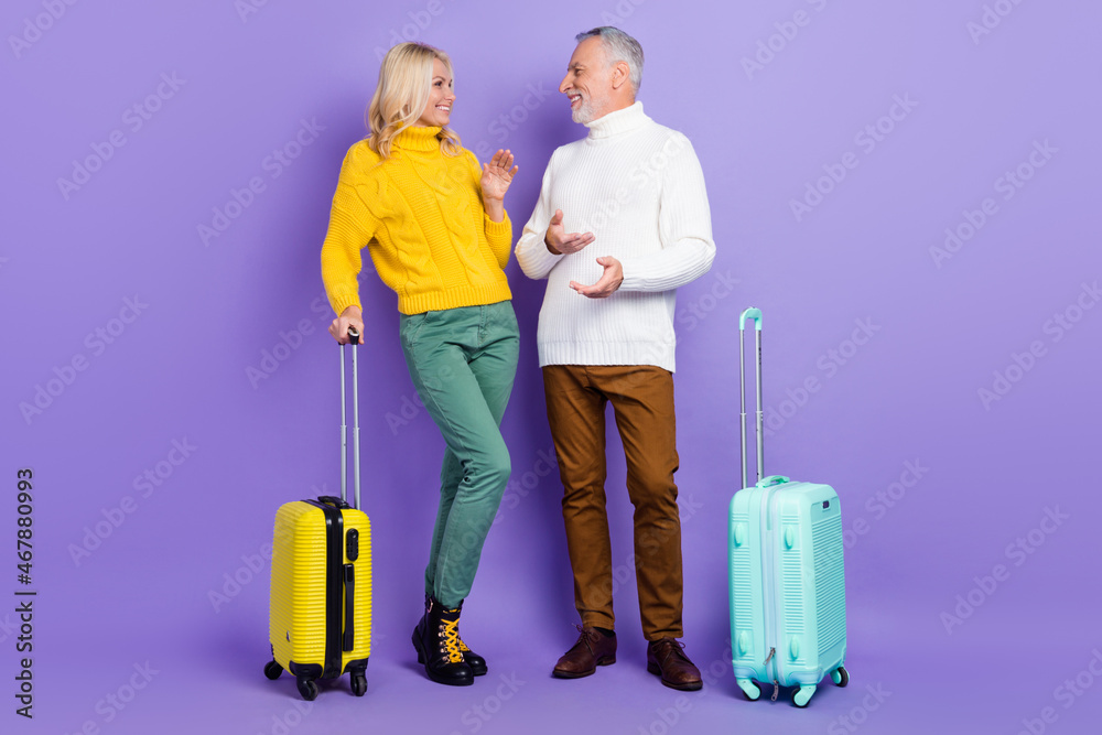 Photo of charming pretty senior husband wife dressed knitwear sweaters holding luggage communicating isolated violet color background Photo of charming pretty senior husband wife dressed knitwear sweaters holding luggage communicating isolated violet color background