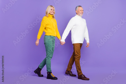 Photo of funny cute senior husband wife dressed knitwear sweaters walking holding arms looking empty space isolated violet color background