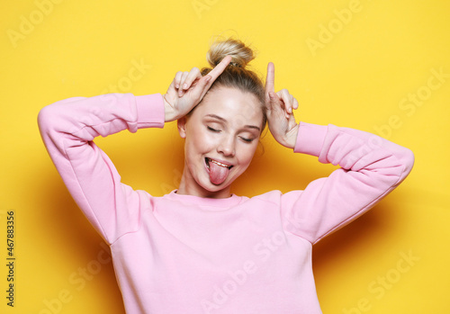 Young woman wearing casual wear over yellow background doing funny gesture with finger over head as bull horns