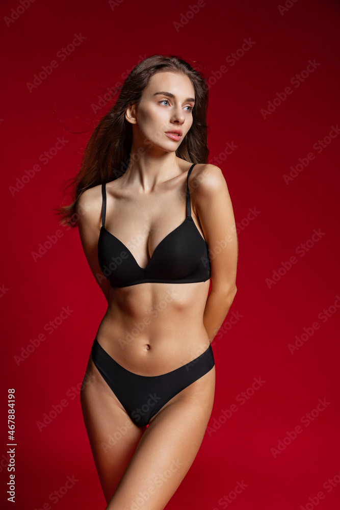 Portrait of young beautiful slim woman in lingerie posing isolated over red studio background. Natural beauty concept.