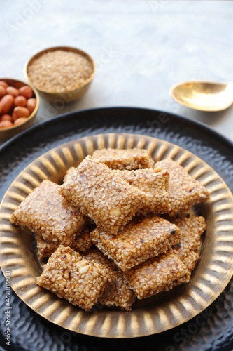  Indian makar sankranti festival food oe sweets. Tilgul in a small brass plate. Tilgul is made out of sesame seeds, peanuts, and jaggery. Til gul chikki or sesame candy. Copy Space.
