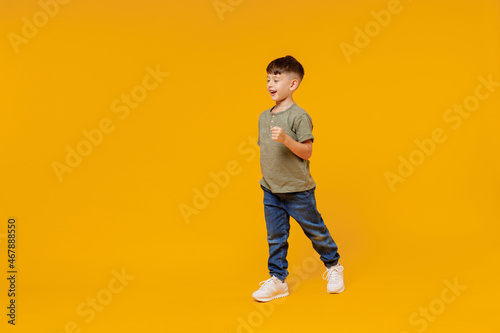 Full body side view little small smiling happy boy 6-7 years old wearing green t-shirt walk go strolling isolated on plain yellow background studio portrait Mother's Day love family lifestyle concept