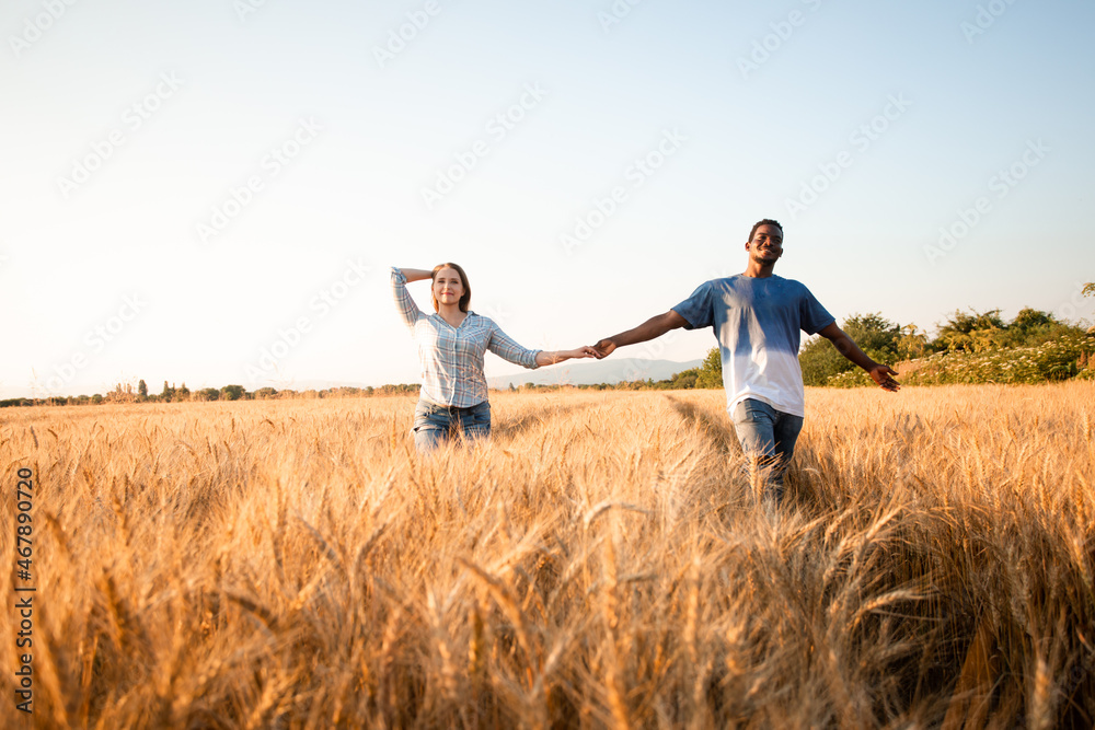 Mixed race young adult couple holding hands while walking in field Mixed race young adult couple holding hands while walking in field