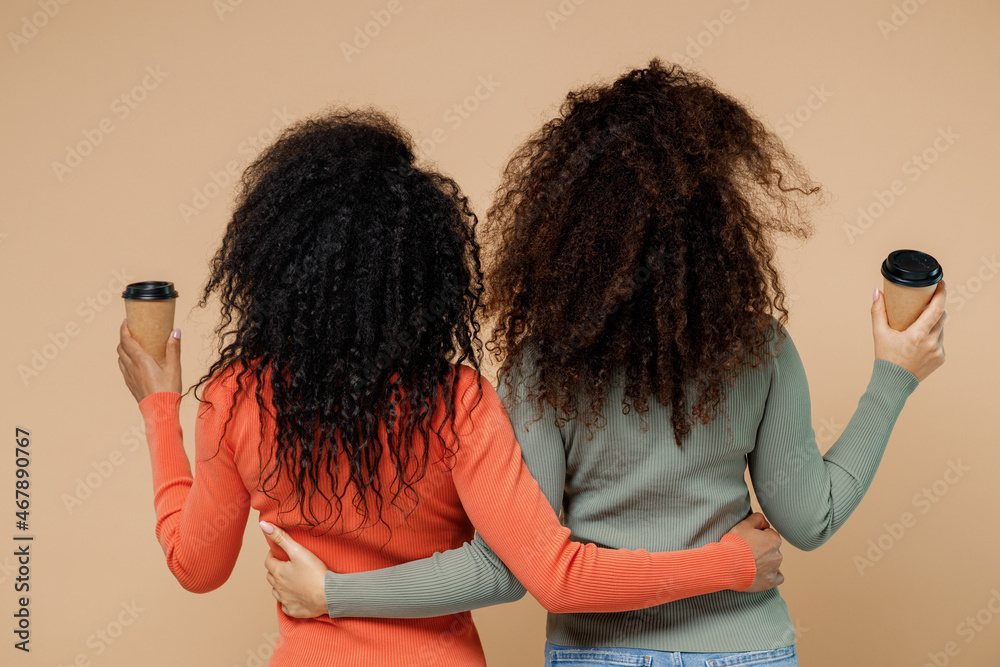 Back rear view two young curly black women friends 20s wear casual shirts clothes hold takeaway delivery craft paper brown cup coffee to go isolated on plain pastel beige background studio portrait. - obrazy, fototapety, plakaty 
