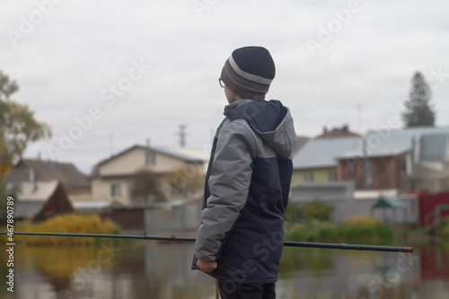 A teenage boy catches a fish with a fishing rod on a river or lake on an autumn cloudy day