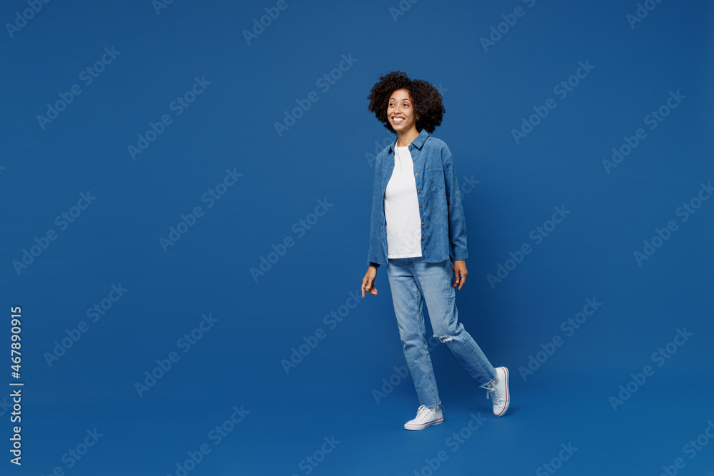 Full body side view fun young smiling happy black woman in casual clothes shirt white t-shirt walking going look aside isolated on plain dark blue background studio portrait. People lifestyle concept.