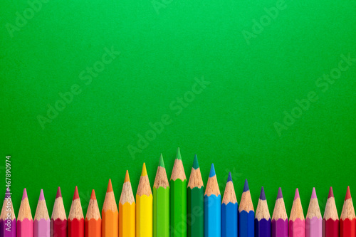 Creative background made of colour pencils on green paper. Flat lay. Education concept.