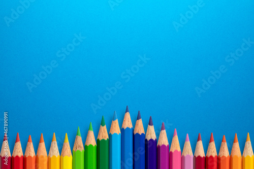 Creative background made of colour pencils on blue paper. Flat lay. Education concept.