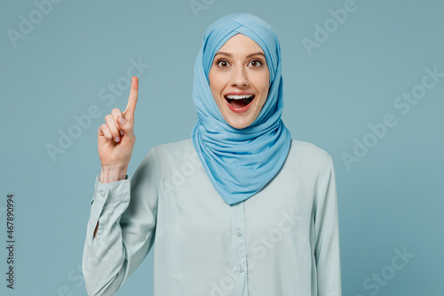 Young arabian asian muslim woman in abaya hijab clothes holding index finger up with great new idea isolated on plain blue background studio portrait People uae middle eastern islam religious concept