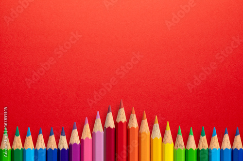 Creative background made of colour pencils on red paper. Flat lay. Education concept.