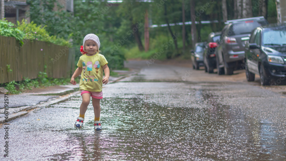 Baby girl walks in the rain through puddles in summer Baby girl walks in the rain through puddles in summer