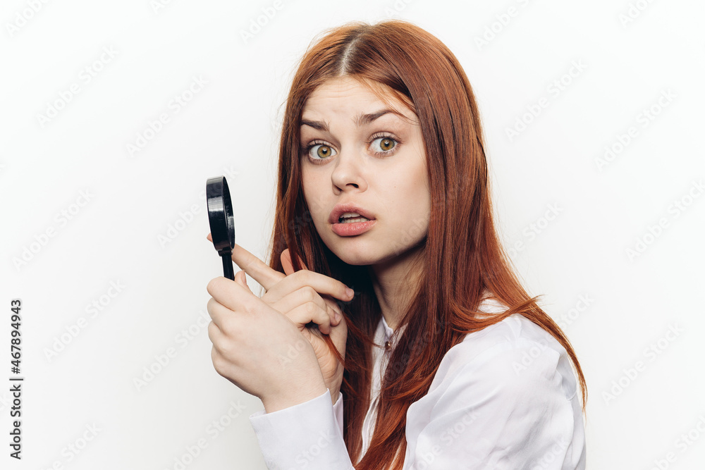 cheerful red-haired woman holding a magnifying glass near her face cheerful red-haired woman holding a magnifying glass near her face