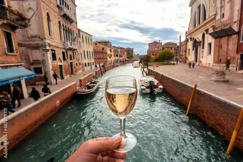 Water canals in Venice and white wine glass in hand of happy tourist