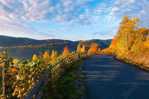 country road at sunrise. beautiful mountain scenery in fall season. trees in colorful foliage along the way. sunny weather with clouds on the sky