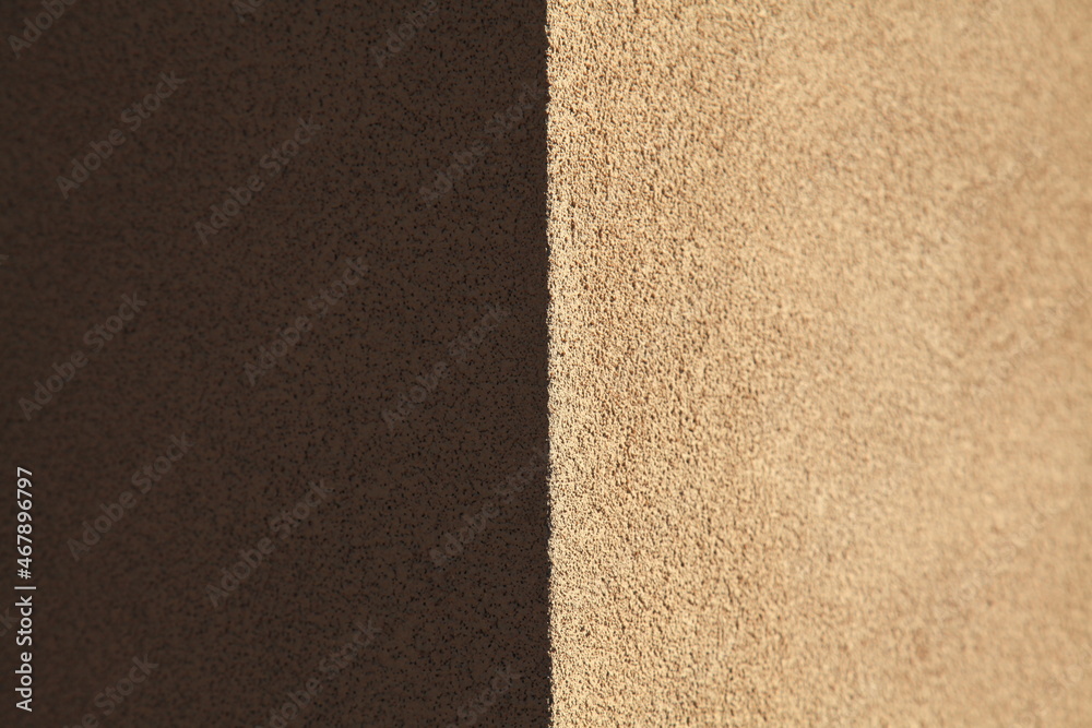 Brown wall texture, background. Structural and rough plaster surface. The corner of a wall or building. Two-component background. Textured coating. Dark and light side. Shady and sunny surface Brown wall texture, background. Structural and rough plaster surface. The corner of a wall or building. Two-component background. Textured coating. Dark and light side. Shady and sunny surface