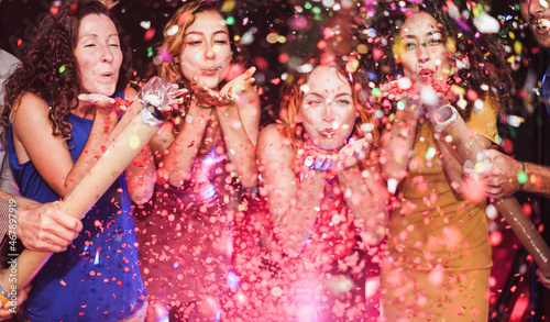 Happy friends celebrating with confetti new year's eve inside disco club - Party concept - Soft focus on left girl hand