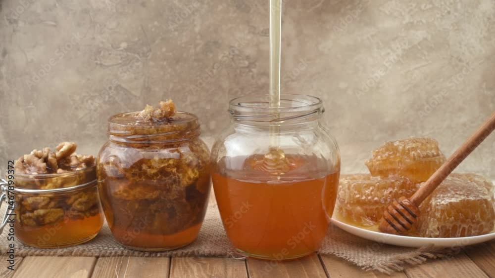 Honey dripping, pouring in glass bowl. Close-up. Assortment of honey products: honeycombs, nuts in honey, beeswax. Flow Healthy organic honey dipping in jar, closeup Honey dripping, pouring in glass bowl. Close-up. Assortment of honey products: honeycombs, nuts in honey, beeswax. Flow Healthy organic honey dipping in jar, closeup