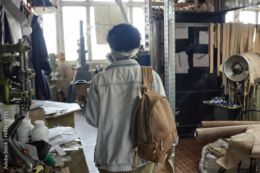 Rear view of African woman with backpack and cup of coffee coming to her work in the workshop