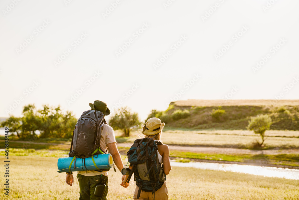 White couple with backpacks holding hands while hiking together outdoors White couple with backpacks holding hands while hiking together outdoors