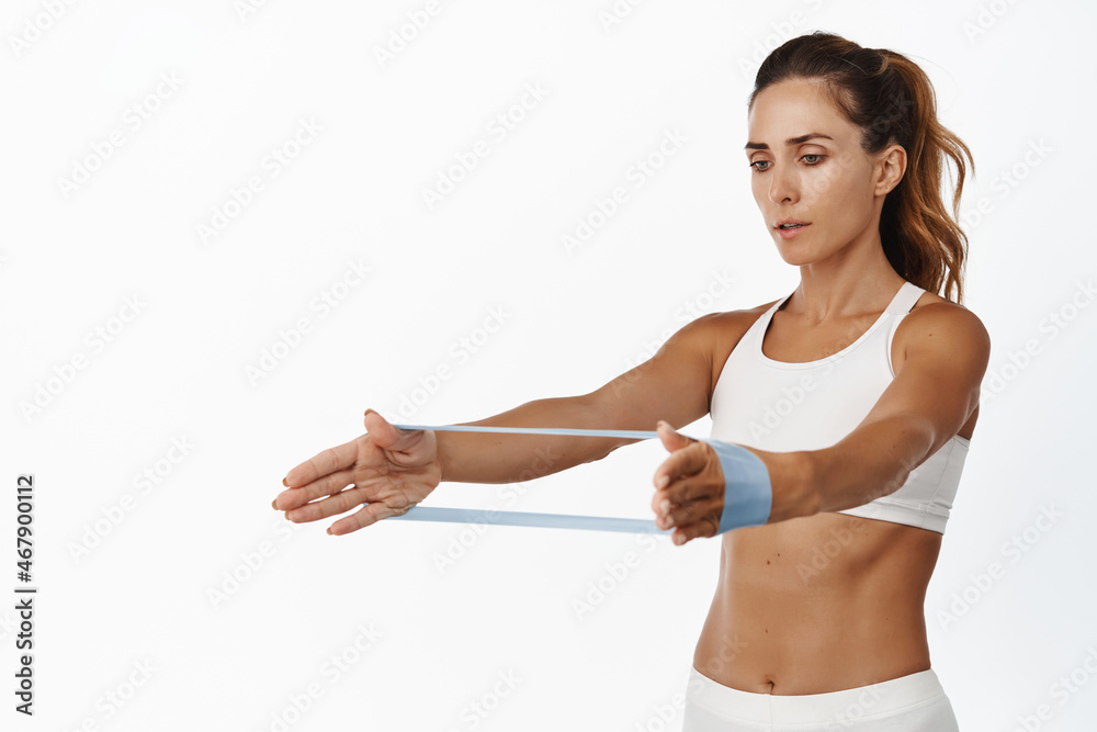 Image of focused female athlete using stretching rope, elastic band workout exercises on arms, standing over white background Image of focused female athlete using stretching rope, elastic band workout exercises on arms, standing over white background