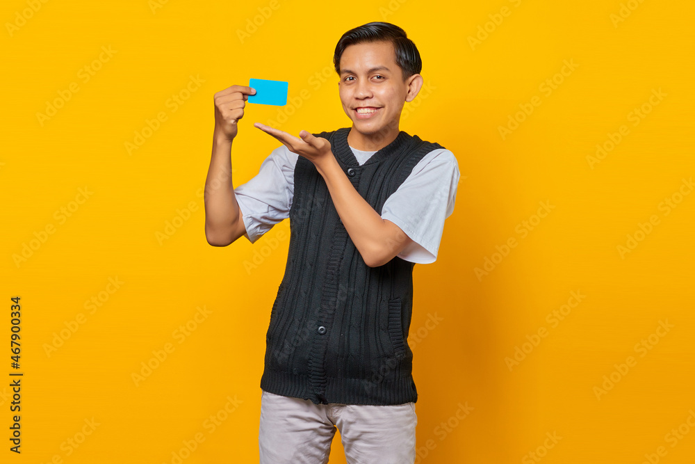 Cheerful Asian man showing credit card over yellow background Cheerful Asian man showing credit card over yellow background
