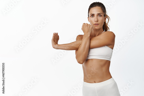 Determined middle aged sportswoman stretching arms, workout and doing fitness exercises for fit body, white background
