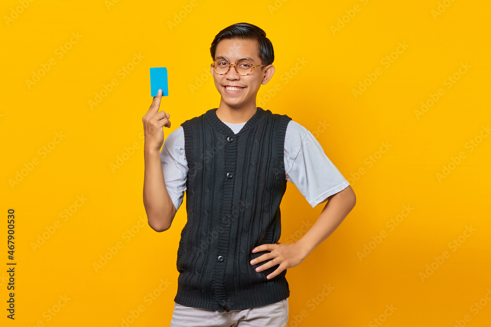 Portrait of attractive Asian man laughing and holding credit card over yellow background Portrait of attractive Asian man laughing and holding credit card over yellow background