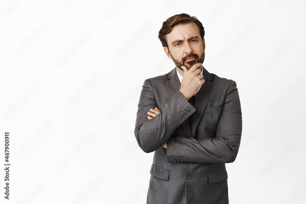 Image of salesman in corporate suit, looking at camera thoughtful, frowning and thinking, making tough choice, white background Image of salesman in corporate suit, looking at camera thoughtful, frowning and thinking, making tough choice, white background