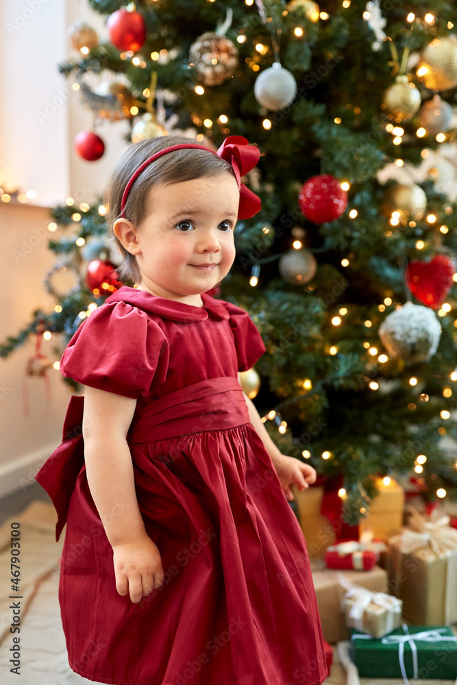 winter holidays and childhood concept - lovely baby girl in red dress over christmas tree at home winter holidays and childhood concept - lovely baby girl in red dress over christmas tree at home