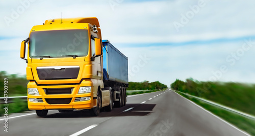 Yellow truck with blue semi-trailer rushes to left on highway. Copy space. Delivery banner.