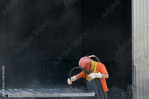 Worker in protective equipment using sandblaster for cleaning surface of metal sheet before painting. Concept of people and industry.  photo