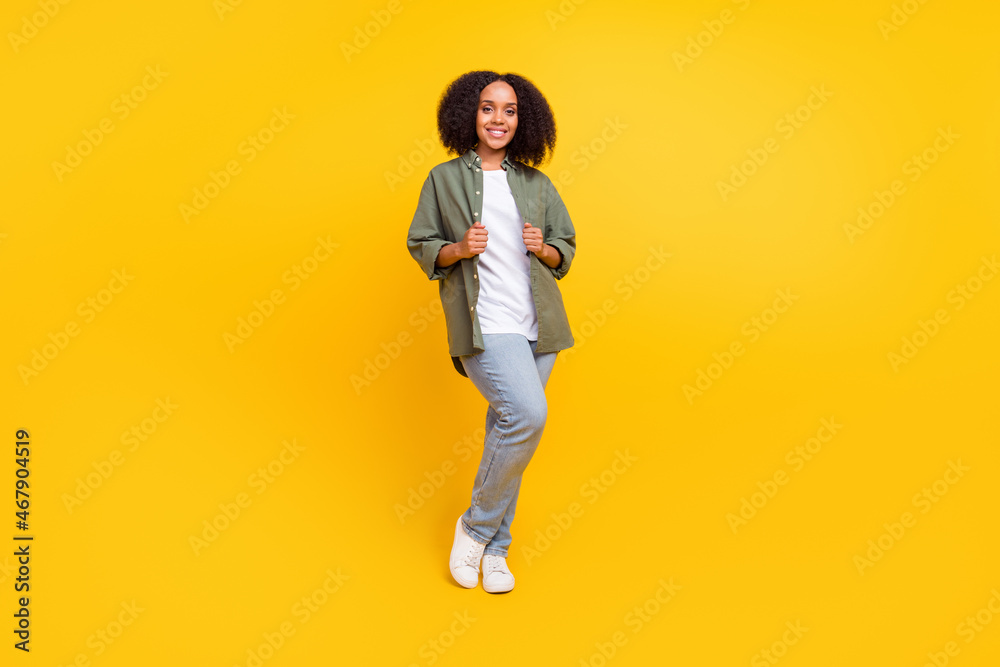 Full size photo of lovely brunette young curvy lady stand wear shirt jeans sneakers isolated on yellow color background Full size photo of lovely brunette young curvy lady stand wear shirt jeans sneakers isolated on yellow color background