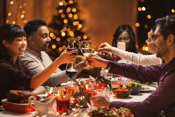 holidays, party and celebration concept - multiethnic group of happy friends having christmas dinner at home and drinking wine