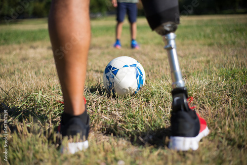 Close-up of father playing football with son. Man with mechanical leg in shorts and little boy in park. Disability, family, love concept photo