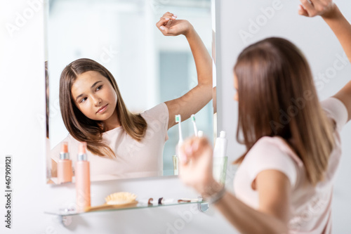 beauty, morning and people concept - teenage girl stretching in front of mirror at bathroom