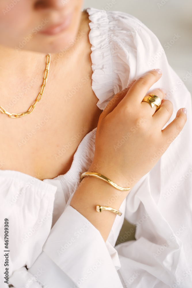Close-up of female hands and neck with gold jewelry, white shirt
