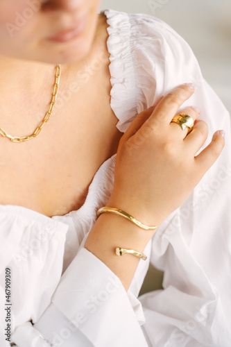 Close-up of female hands and neck with gold jewelry, white shirt