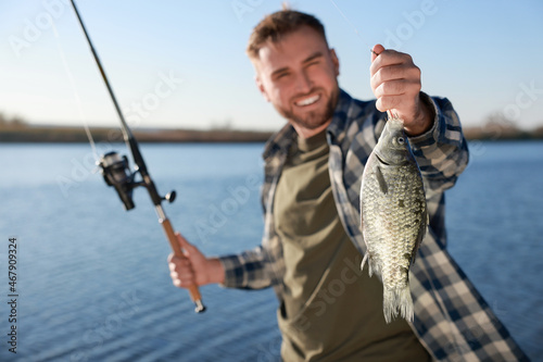 Fisherman with fishing rod at riverside, focus on catch