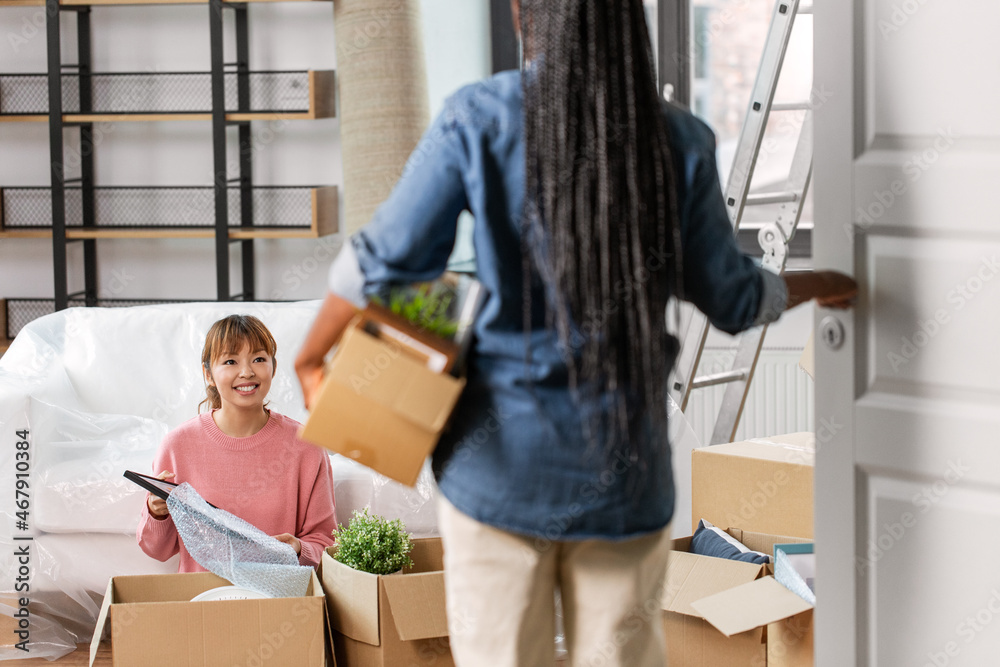 moving, people and real estate concept - woman unpacking boxes and her friend entering room at new home moving, people and real estate concept - woman unpacking boxes and her friend entering room at new home