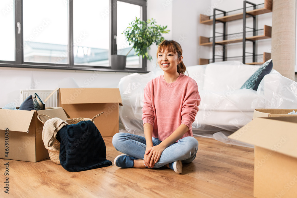 moving, people and real estate concept - happy smiling woman with boxes sitting on floor at new home