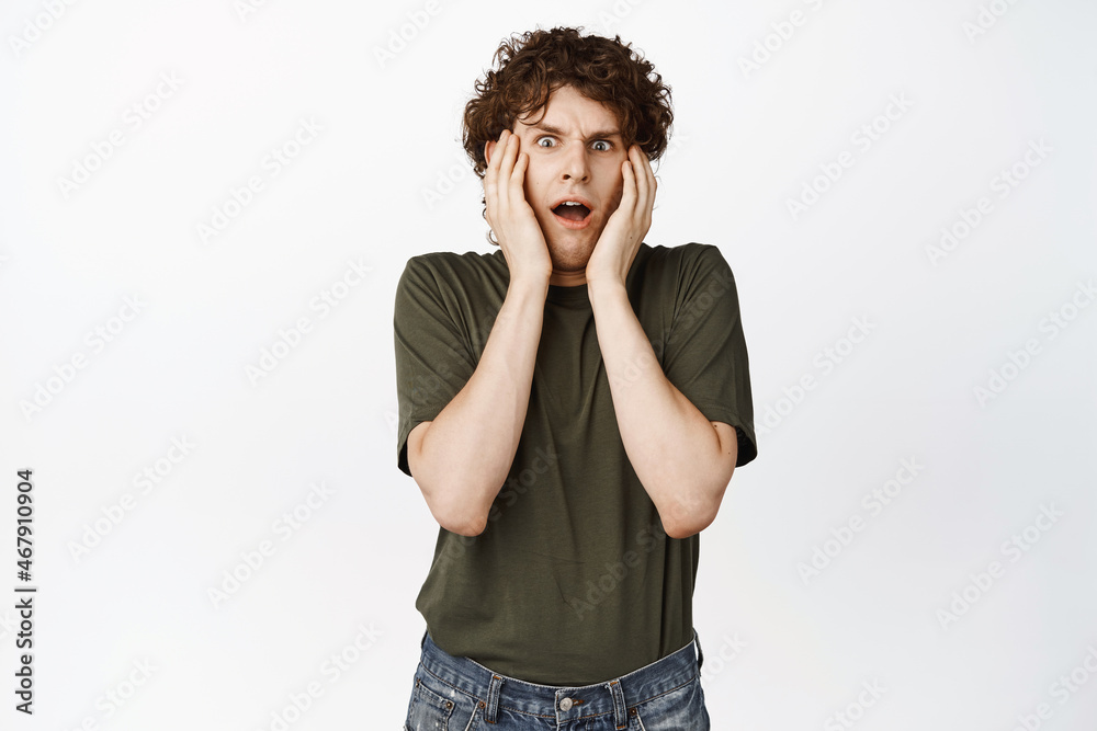 Scared and anxious curly guy freak out, screaming from fear and staring at camera shocked, standing over white background Scared and anxious curly guy freak out, screaming from fear and staring at camera shocked, standing over white background
