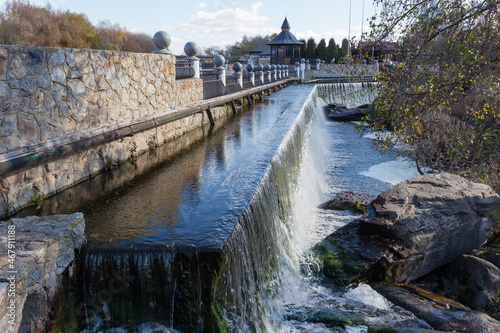 Artificial waterfall formed by the concrete dam in autumn park