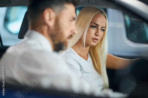 Competent car dealer showing female customer interior of luxury auto. Caucasian man and woman sitting inside and talking. Concept of selling and purchase.